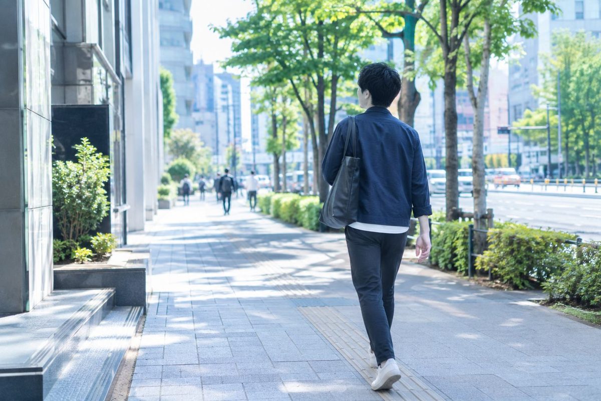 街路樹のある歩道を歩く男性の後ろ姿